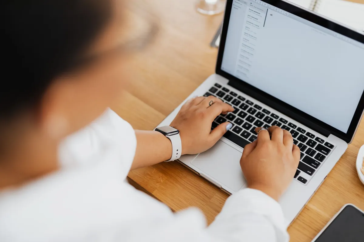 Woman typing a document on a laptop at a wooden desk