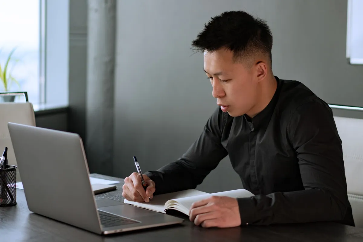Office worker taking notes while working on a laptop