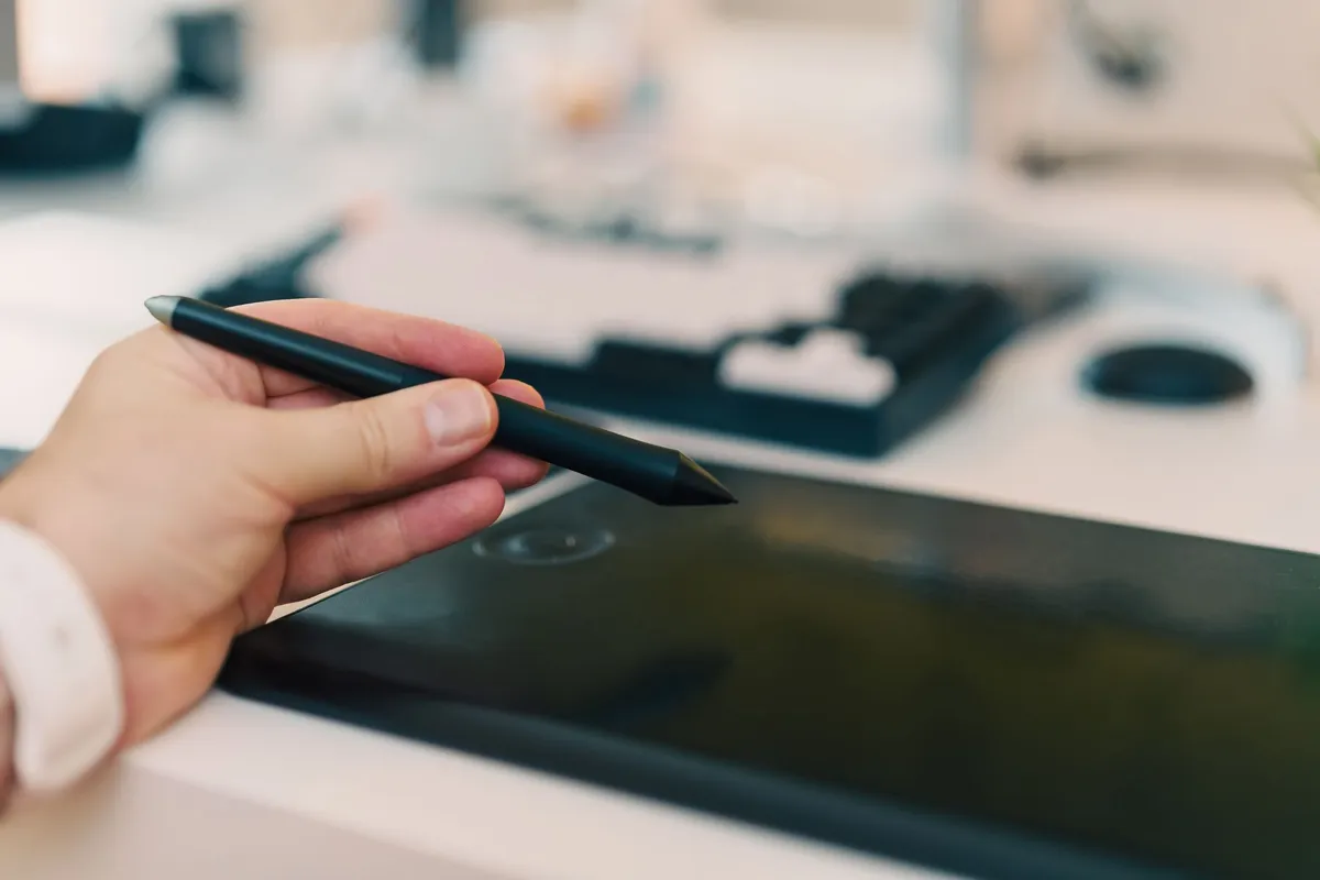 Hand holding a stylus above a graphics tablet