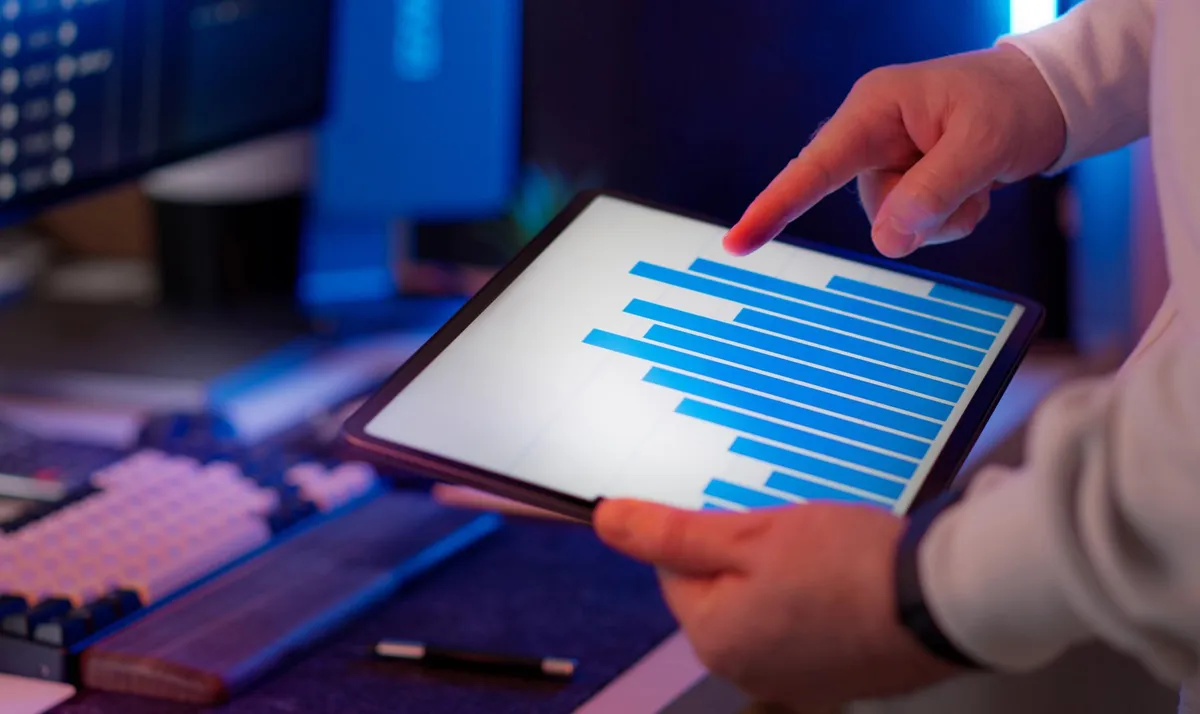 Hand pointing at a bar chart on a tablet at a desk