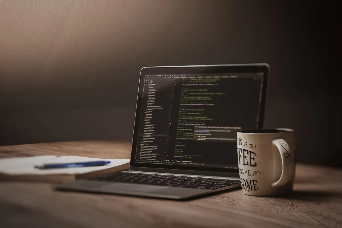 Laptop showing code beside a notebook and coffee mug