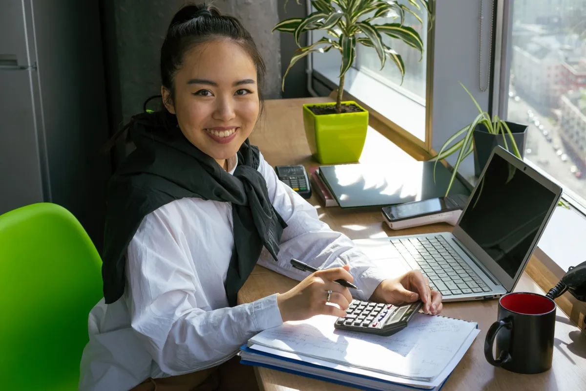 Smiling business owner doing accounts with a calculator and laptop